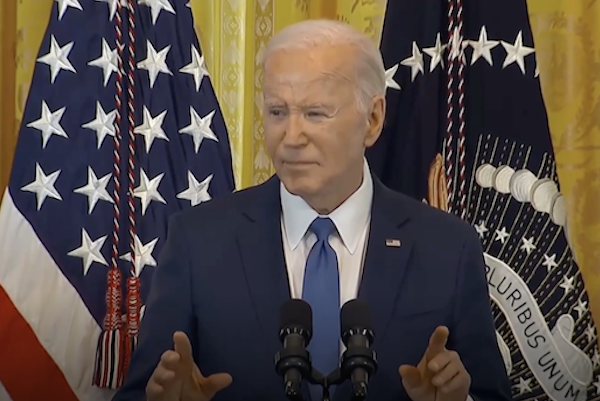 President Biden standing at the podium with microphones up against US flags background.