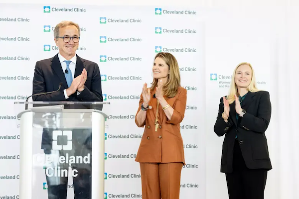 Maria Shriver & individuals in business attire applauding at a Cleveland Clinic podium.