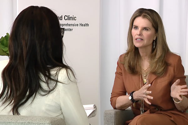 Maria Shriver in a seated interview, gesturing with hands, in a clinic setting.